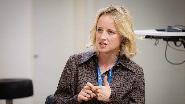 Eine Person mit Headset-Mikrofon sitzt auf dem Podium und spricht gestikulierend während einer Diskussion.