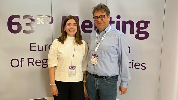 Die beiden Vertreter:innen der österreichischen Kommissionsbehörde KommAustria posieren für die Kamera vor einer Wand mit den Logos und Schriftzügen des 63. EPRA Meetings. 
