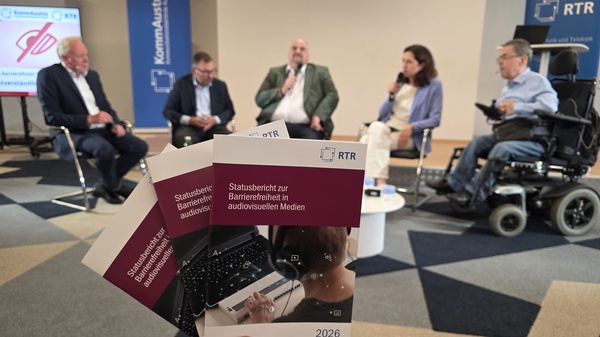 Der Statusbericht zur Barrierefreiheit in audiovisuellen Medien 2026 im Vordergrund, im Hintergrund die Podiumsdiskussion.
