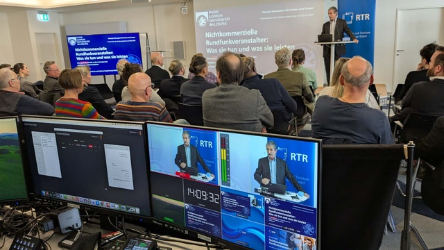 Prof. Trappel auf der Bühne, im Vordergrund auf Monitoren der Internet-Übertragungstechnik