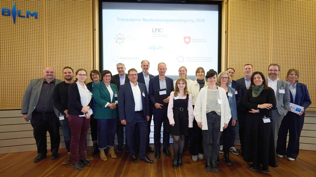 Gruppenfoto der Teilnehmer:innen der Transalpinen Medienkompetenztagung vor einer Präsentationsfolie mit unterschiedlichen Logos darauf.