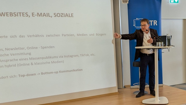 Josef Kalina, Unternehmer, PR-Berater und ehemaliger Politiker im Vortrag, zeigt auf Leinwand mit Präsentationsfolie