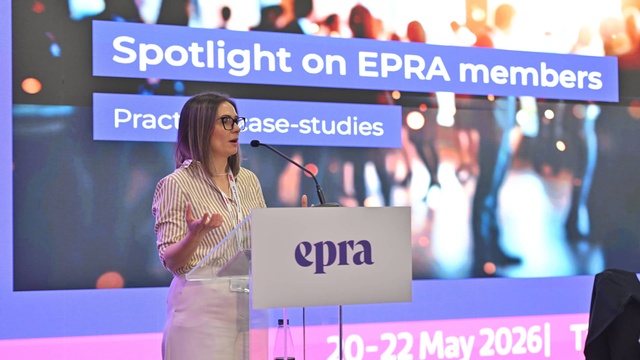 Eine Referentin präsentiert am EPRA-Rednerpult einen Praxisbericht zu Mitgliedsprojekten. Hinter ihr ist die Präsentationsfolie „Spotlight on EPRA members“ zu sehen.