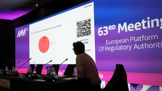 Auf einer großen Leinwand werden die Ergebnisse einer Live-Umfrage mit Kreisdiagramm und QR-Code präsentiert. Ein Teilnehmer betrachtet die Auswertung von der Bühne aus.