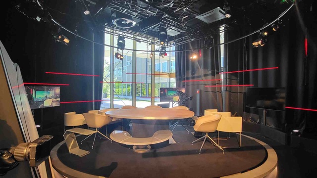 Ein modern eingerichtetes Fernsehstudio mit Kameras, Beleuchtungstechnik und einem runden Besprechungstisch. 