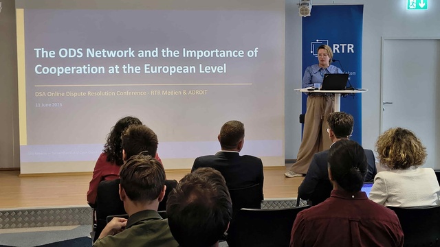 Referentin spricht an einem Rednerpult vor einer Präsentationsfolie zur europäischen Zusammenarbeit im ODS-Netzwerk; Teilnehmende verfolgen den Vortrag.