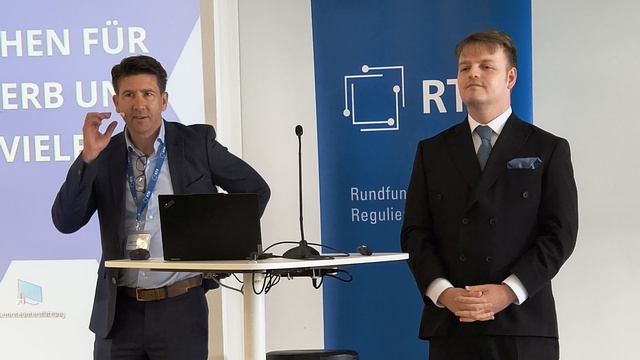 Moderator steht neben dem Rednerpult während einer Präsentation.