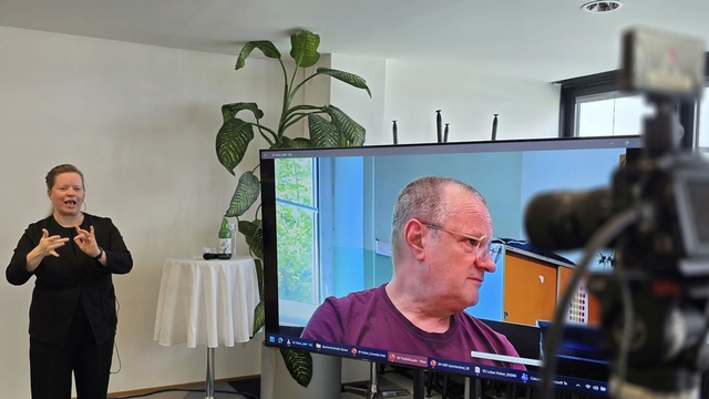 Gebärdensprachdolmetscherin begleitet die hybride Veranstaltung zur Barrierefreiheit in audiovisuellen Medien.