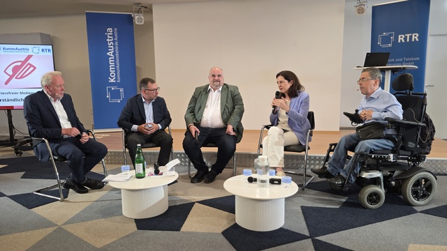 Expert:innen diskutieren auf einem Podium über Barrierefreiheit in audiovisuellen Medien. Ein Teilnehmer nimmt im Elektrorollstuhl an der Diskussion teil.