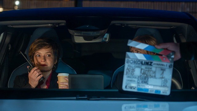 Zwei Frauen sitzen bei Dreharbeiten in einem Auto; im Vordergrund ist eine Filmklappe zu sehen.