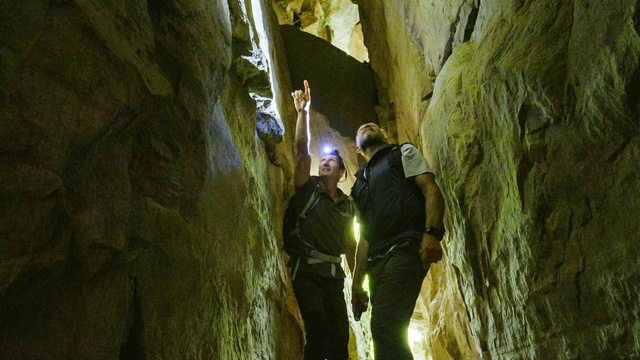 Zwei Männer erkunden mit Stirnlampen eine enge Felsspalte und betrachten die steilen Felswände.