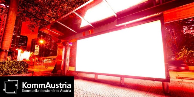 Ein beleuchtetes Citylight an einer Bushaltestelle in der Großstadt bei Nacht, das Themenbild für Veröffentlichungen der KommAustria.